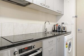 A compact kitchen with a stainless steel oven, a built-in washing machine, and a sink. - Stylish Apartment 130m to Int Conference Centre (Auckland CBD)