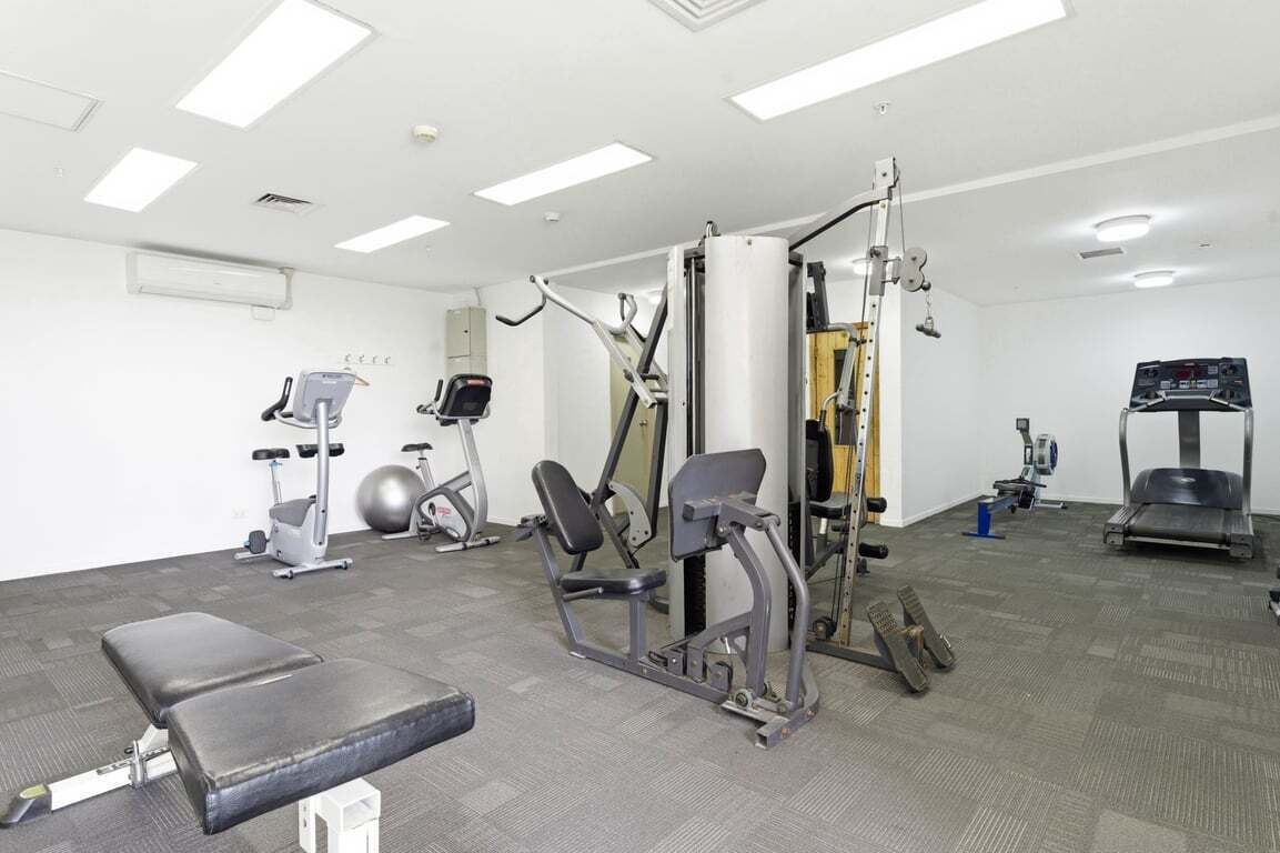 Ein Fitnessstudio mit verschiedenen Trainingsgeräten, einer Bank und einem Laufband.