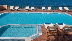 A pool with lounge chairs, a smaller pool, and a view of the ocean.