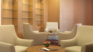 A hotel lobby with two armchairs, a central white chair, a small table with a magazine and a flower vase, and wooden paneling on the walls. - Sama-sama Express Klia 2 (Sepang)