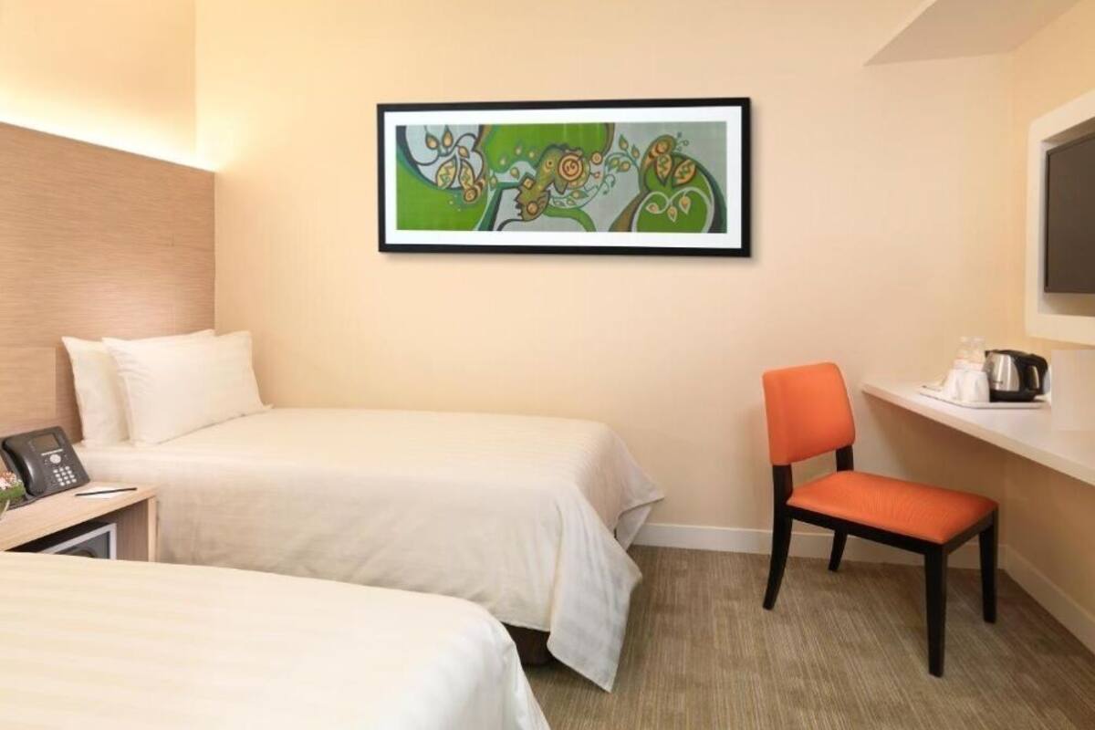 A hotel room with two beds, a desk with a phone, a chair, a painting on the wall, and a coffee maker on the counter.