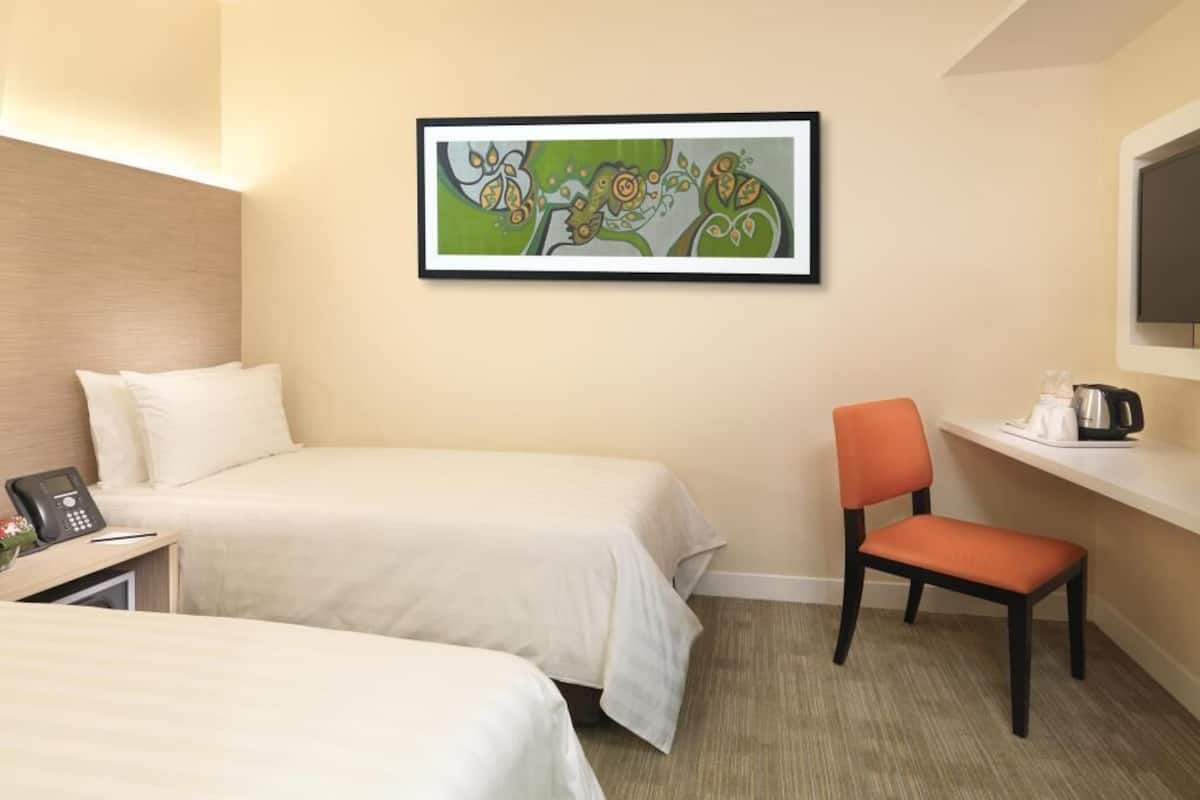 A hotel room with two beds, a chair, a desk with a phone, a coffee maker, and a framed abstract painting on the wall.