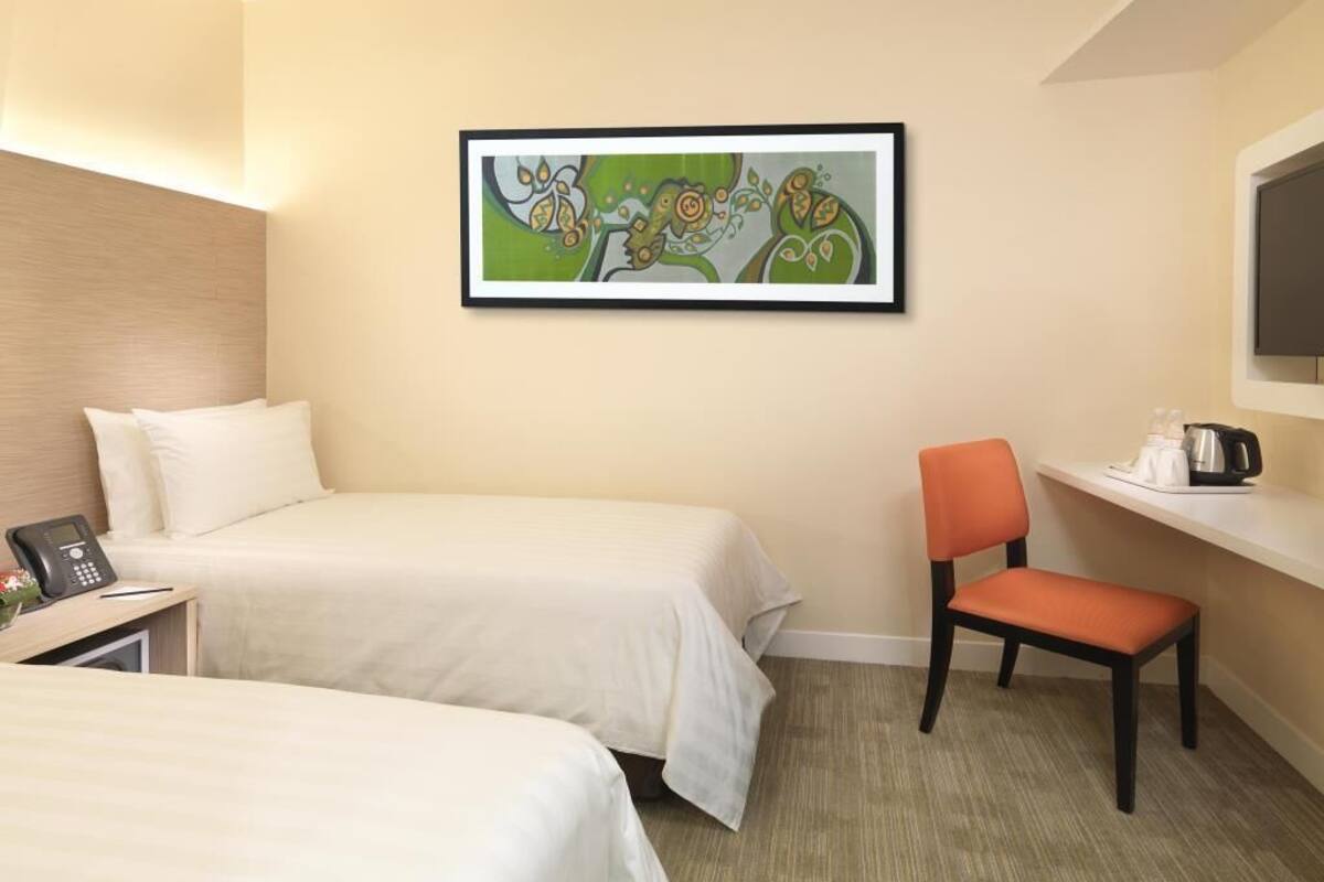 A hotel room with two beds, a chair, a desk with a phone, a coffee maker, and a framed abstract painting on the wall.
