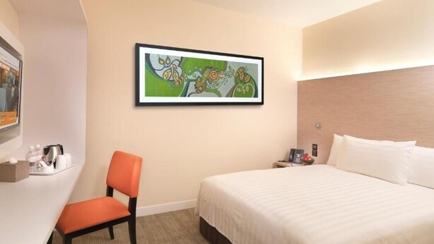 A hotel room with a bed, a desk with a chair, a painting on the wall, and a nightstand with a lamp. - Sama-sama Express Klia 2 (Sepang)