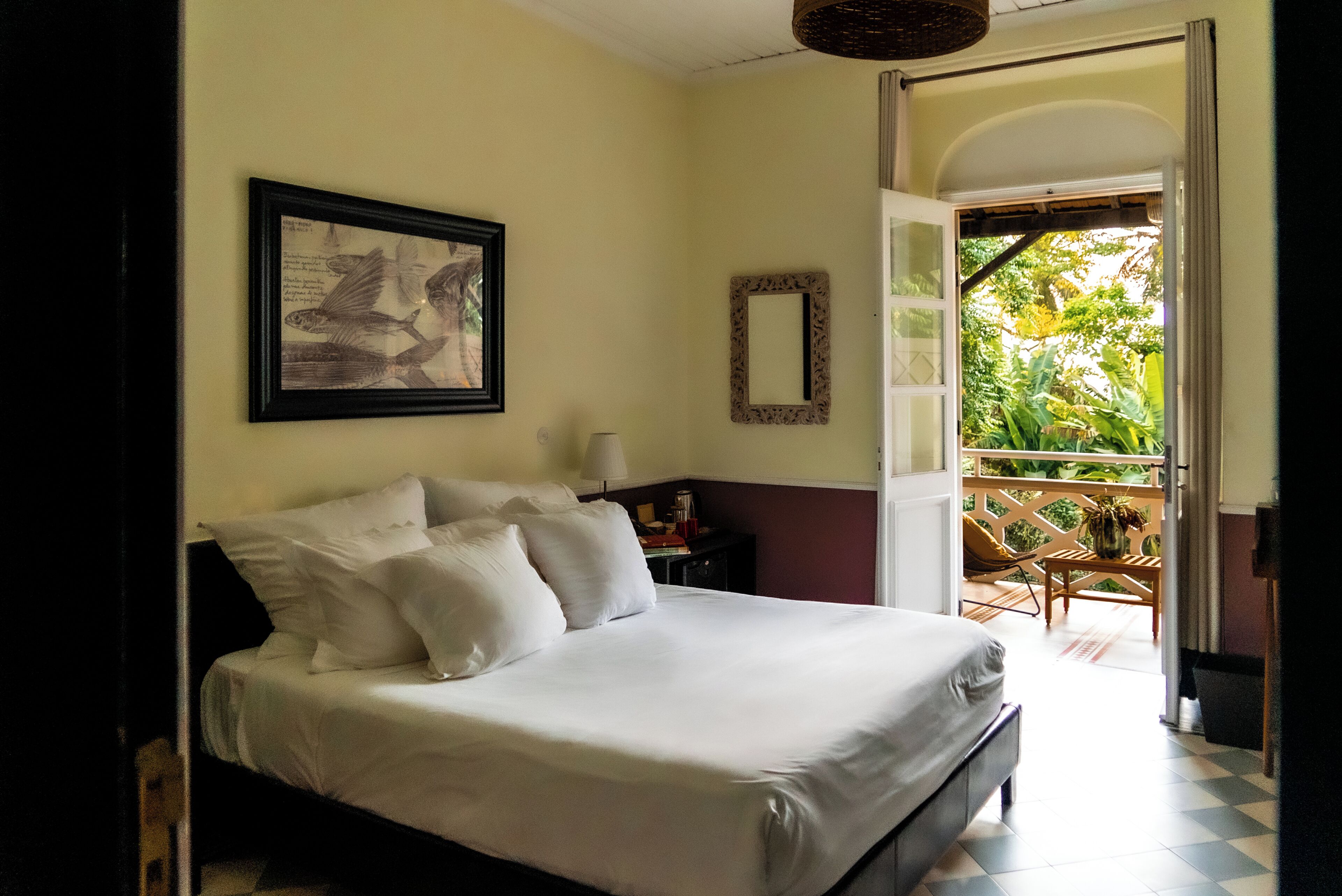 A bedroom with a bed, a framed picture, a mirror, and a view of a balcony with plants.