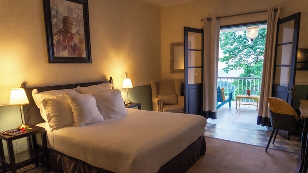 Une chambre d’hôtel avec un grand lit, deux tables de chevet avec des lampes, une chaise et un balcon donnant sur la forêt.