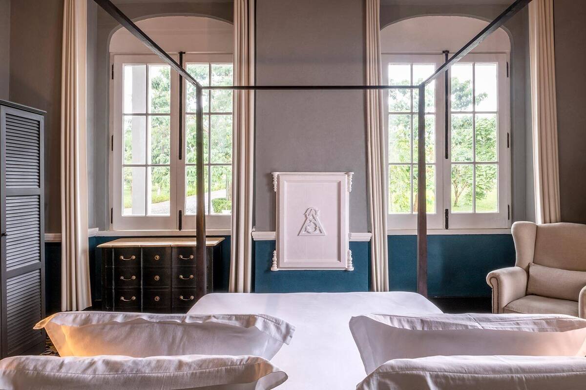 A room with a bed, two chairs, a dresser, and a framed picture on the wall.