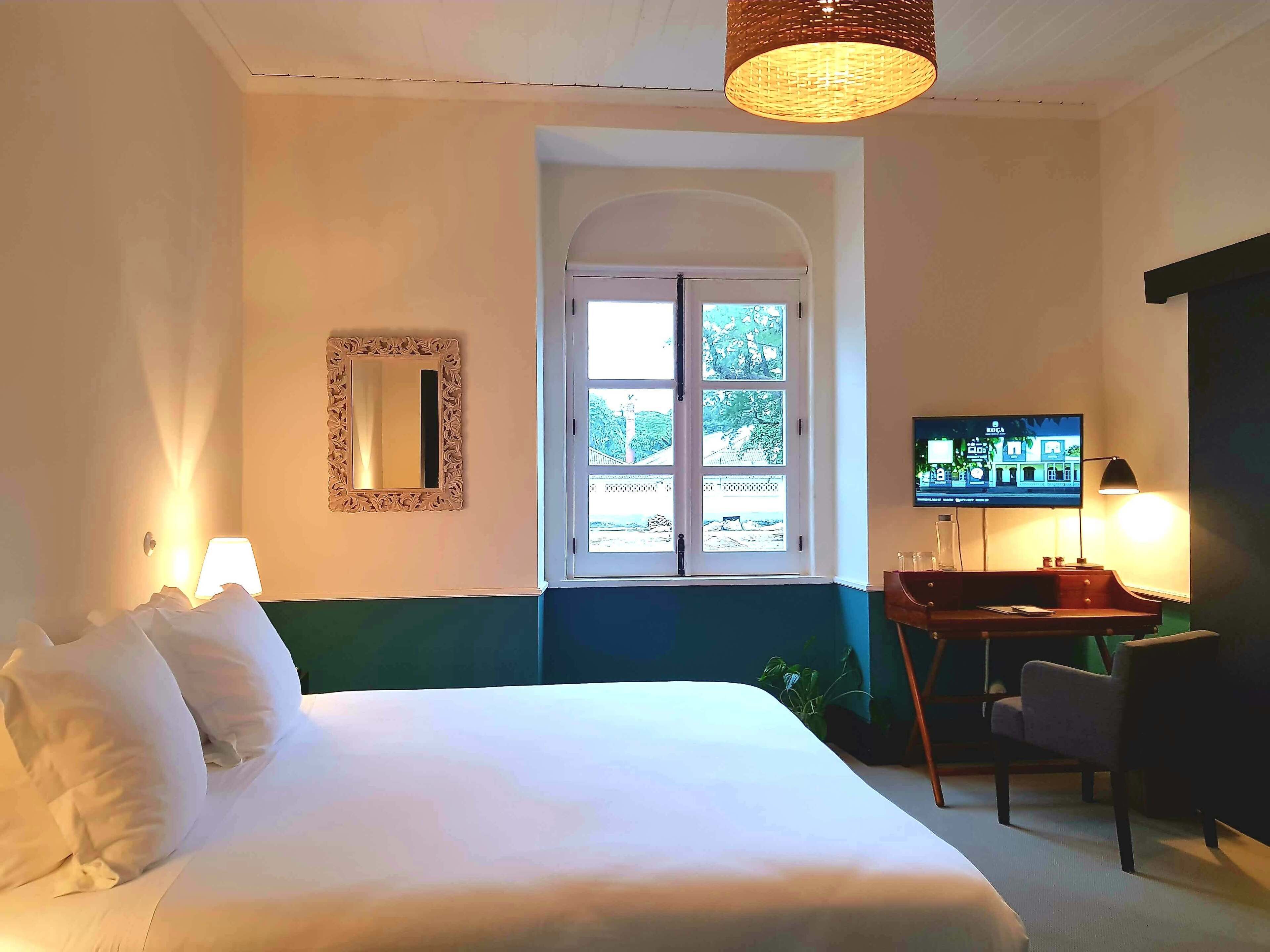 A hotel room with a bed, a television, a desk with a chair, a window with a view, and a mirror on the wall.