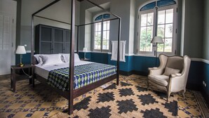 Un lit à baldaquin avec une couvre-lit à motifs, une chaise et une grande fenêtre avec des volets.