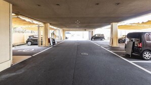 Área de estacionamento coberta com vários carros estacionados, um caminho central e vista da rua na extremidade aberta.