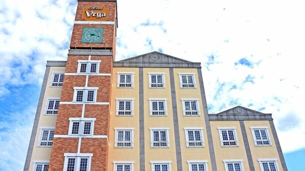 Um edifício de vários andares com uma torre de relógio, diversas janelas e uma placa com o texto 'Kon Vegia'.