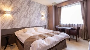 Quarto de hotel com cama, mesa pequena, duas cadeiras, parede de mármore e janela com cortinas.