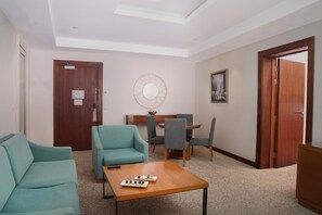 Ein Hotelzimmer mit einer Couch, einem Esstisch mit Stühlen, einem runden Spiegel und einer Deckenleuchte.