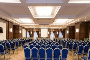 A conference room with rows of blue chairs, a large screen, and a ceiling with recessed lighting. - Gewan Hotel Cairo (Giza)