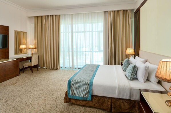 A hotel room with a bed, bedside lamps, a desk, a chair, a TV, and a large window with curtains. - Gewan Hotel Cairo (Giza)