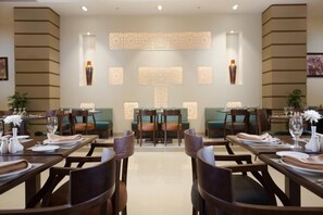 A restaurant with multiple tables, chairs, and a decorative wall with light fixtures. - Gewan Hotel Cairo (Giza)