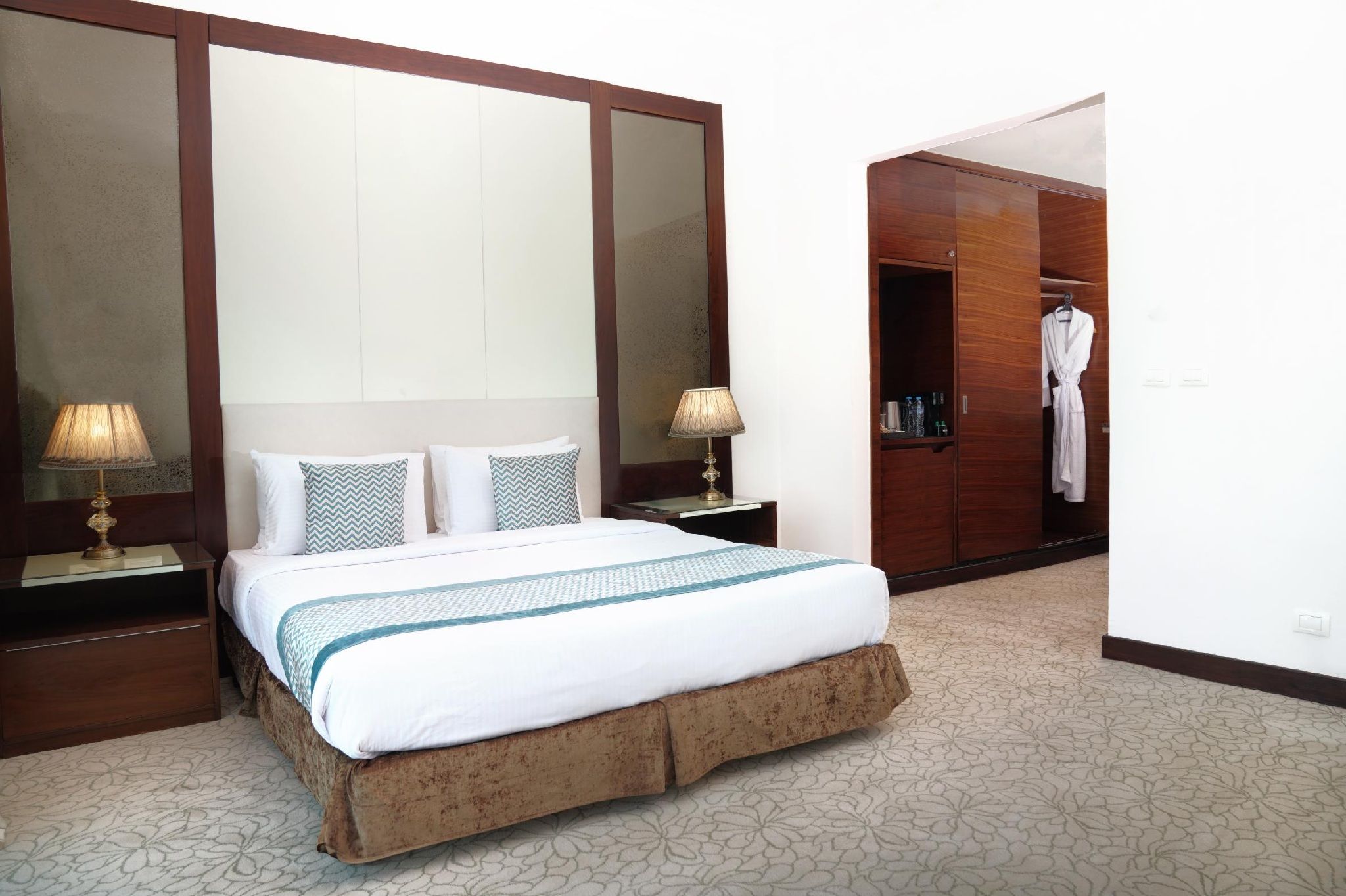 A hotel room with a bed, two bedside tables, a wardrobe, and a mirror.