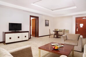 A hotel room with a TV, a dining area, a sofa, and a table with fruit. - Gewan Hotel Cairo (Giza)