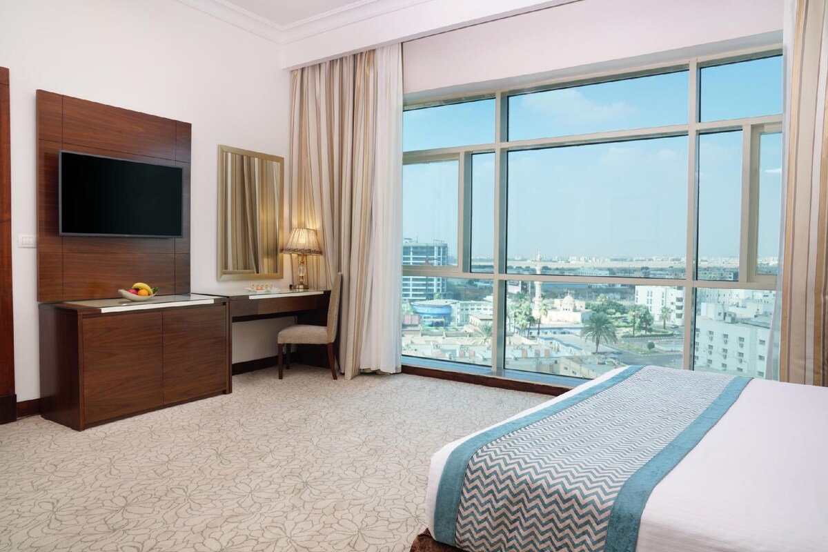 A hotel room with a large window, a flat-screen TV, a desk, and a bed.