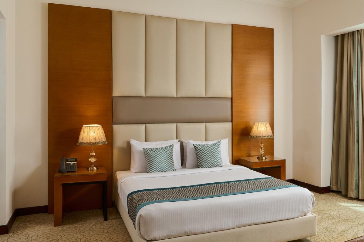A hotel room with a large bed, two bedside tables with lamps, a telephone, and a patterned rug.