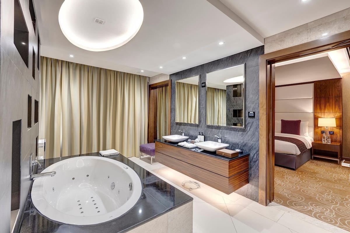Un baño de hotel moderno con una bañera grande, dos lavamanos, un tocador y un espejo.