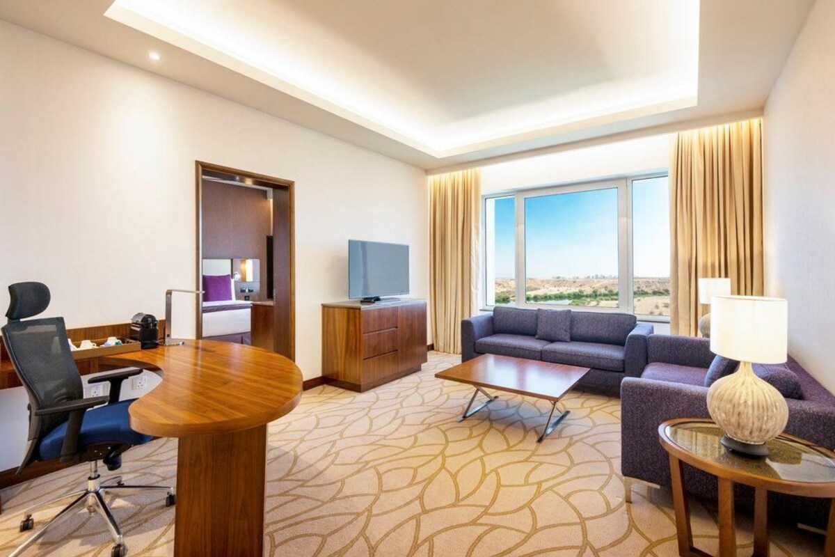 A hotel room with a conference table, a sofa, a television, and a large window with a desert view.