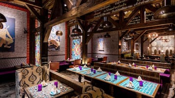 A restaurant with wooden beams, patterned walls, and tables set for dining.