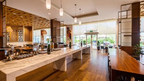 A modern restaurant with a marble counter, wooden flooring, pendant lighting, and large windows offering a view of the outdoors.