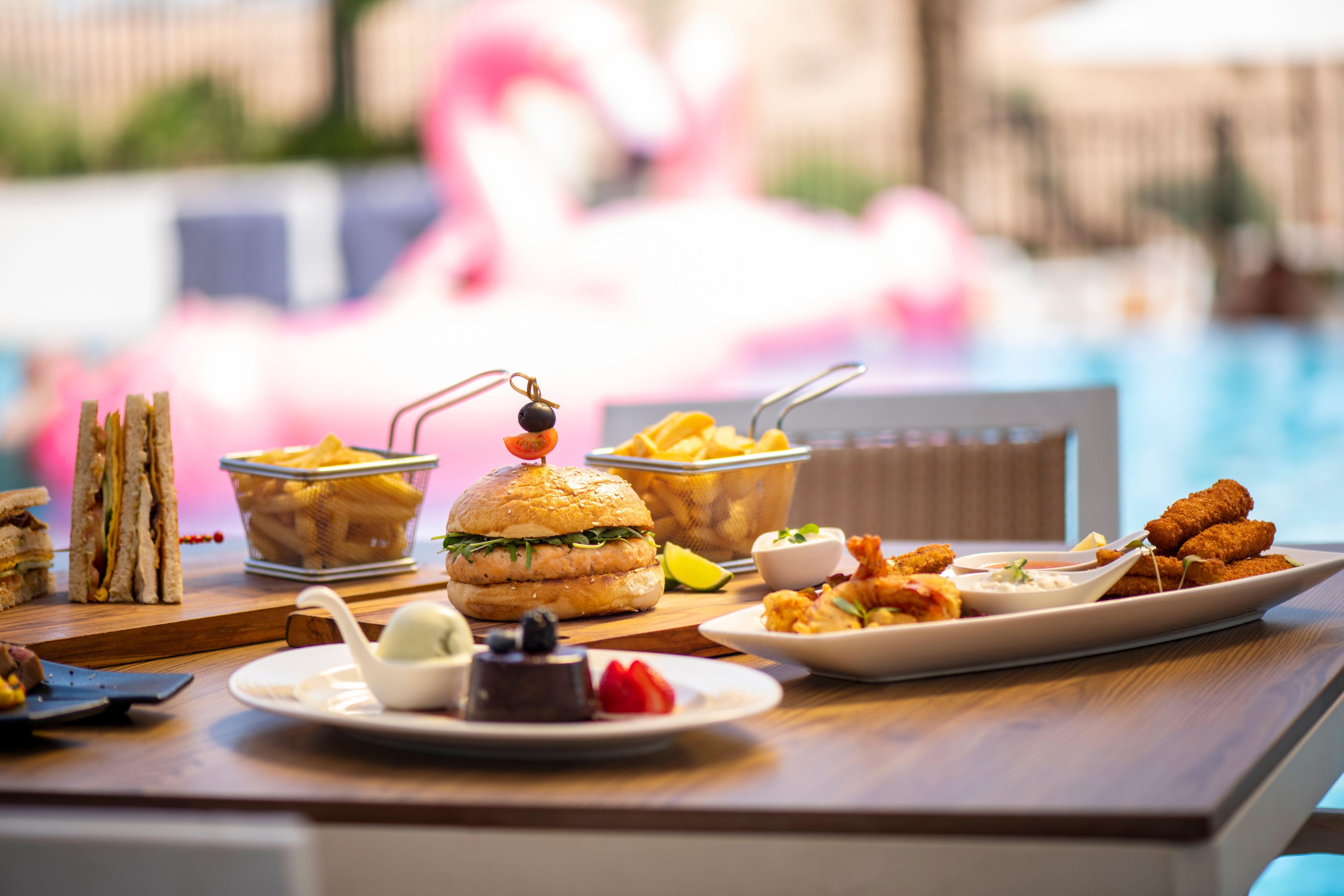 Una mesa de comedor con diversos alimentos, como sándwiches, hamburguesas y aperitivos fritos.
