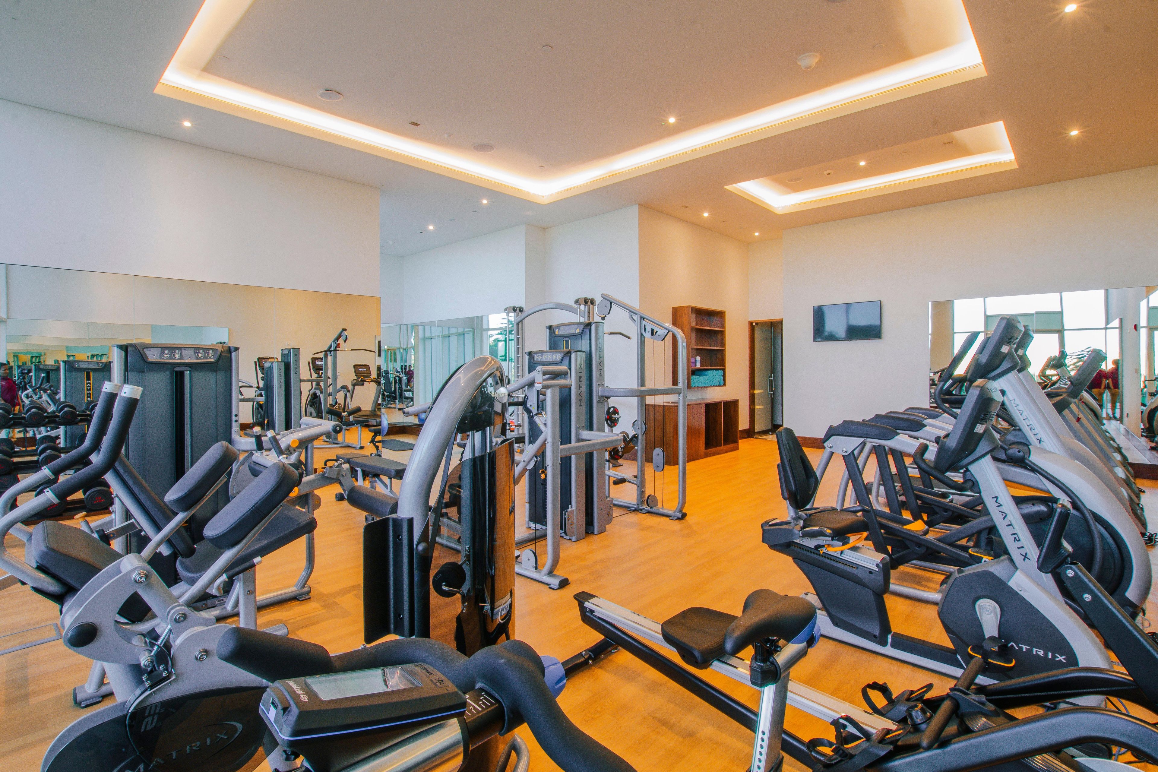 Un gimnasio con varias máquinas de ejercicio, un televisor y piso de madera.