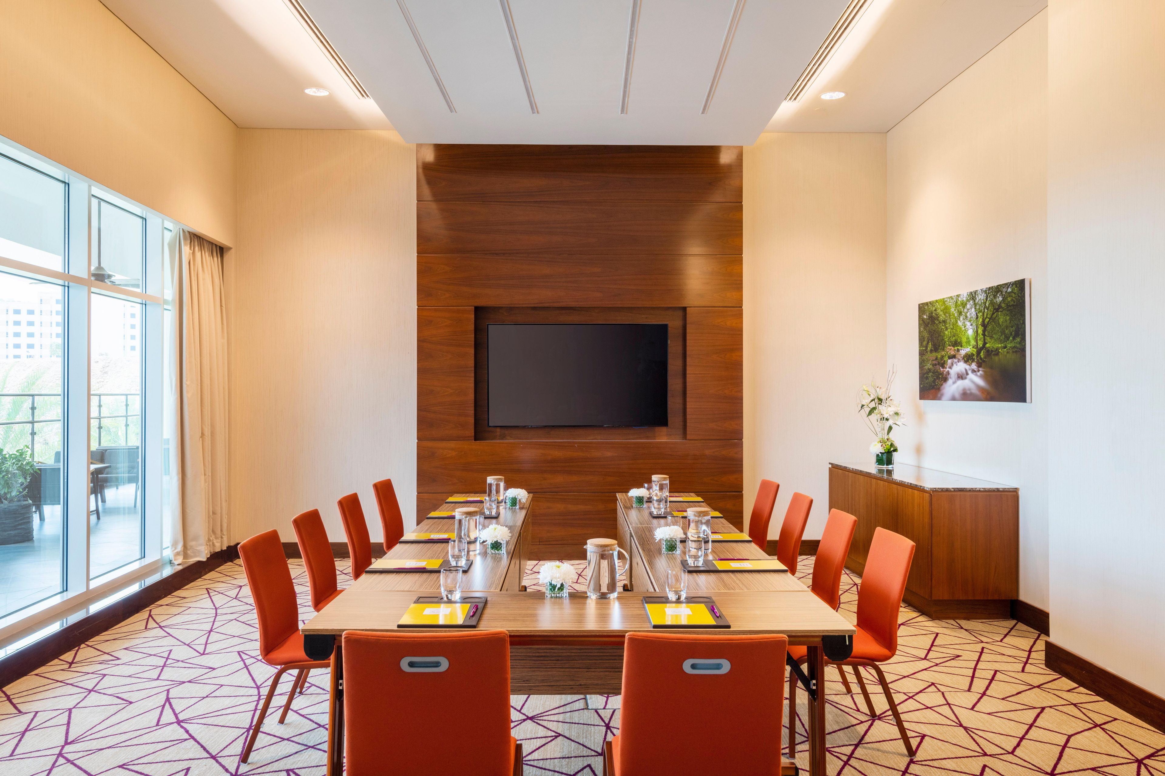A conference room with a large table, chairs, a TV, and a window.