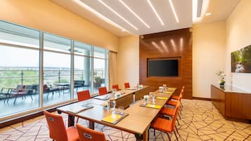 Un salón de conferencias con una larga mesa, sillas anaranjadas, un televisor de pantalla plana y amplias ventanas con vistas.