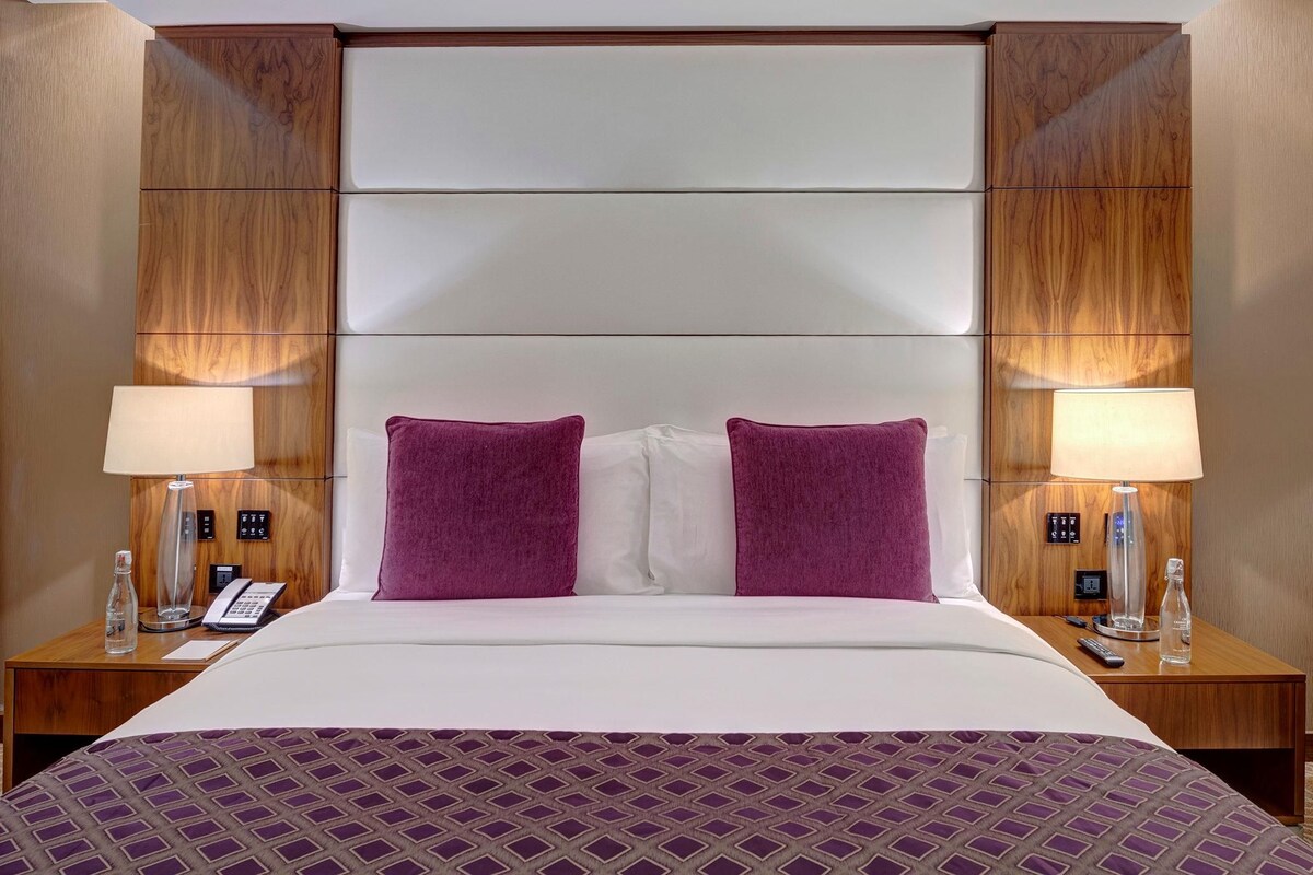 A hotel room with a large bed, two nightstands, a telephone, lamps, and a wooden headboard.