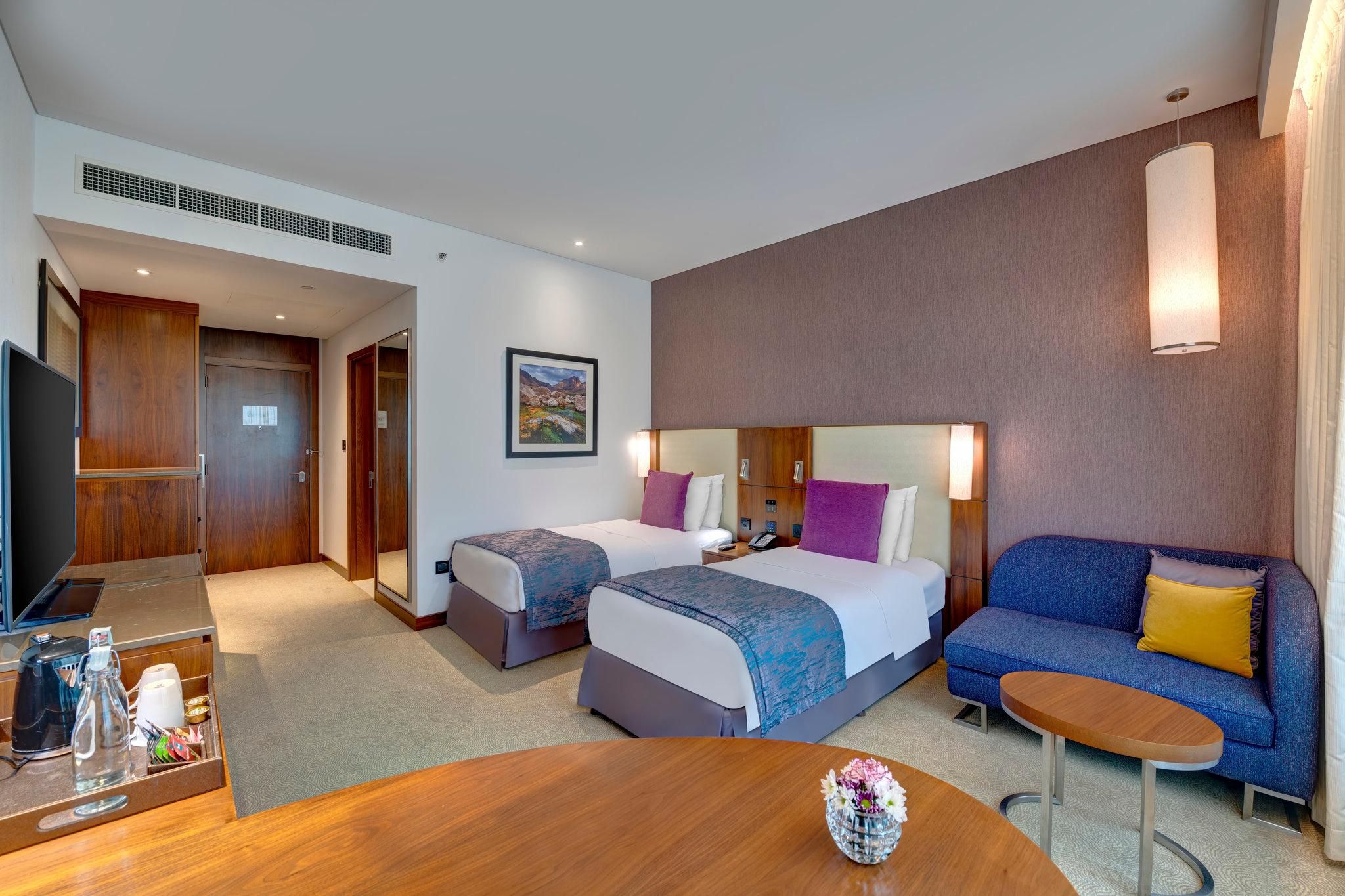 Habitación de hotel con dos camas, un sofá, una mesa de centro y una televisión.