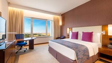Quarto de hotel com uma cama grande, uma escrivaninha, uma cadeira, uma televisão e vista para o deserto.