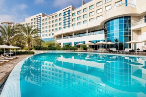A hotel with a large swimming pool, sun loungers, and palm trees. - Crowne Plaza Muscat Ocec (Muscat)