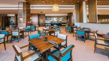 Un restaurante con mesas de madera y sillas azules, una zona de bar y un techo con vigas de madera.