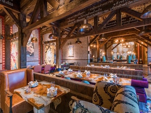 A restaurant with wooden beams, tables with cutlery, and patterned cushions. - Crowne Plaza Muscat Ocec (Muscat)