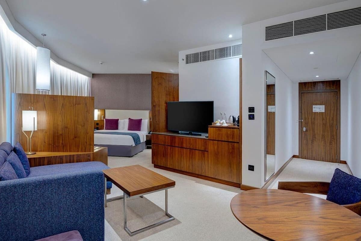 Una habitación de hotel moderna con un sofá, una mesita, un televisor, una cama y un armario de madera.