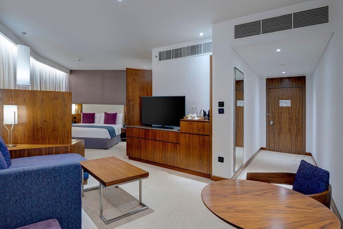 A modern hotel room with a sofa, a small table, a TV, a bed, and a wooden cabinet.