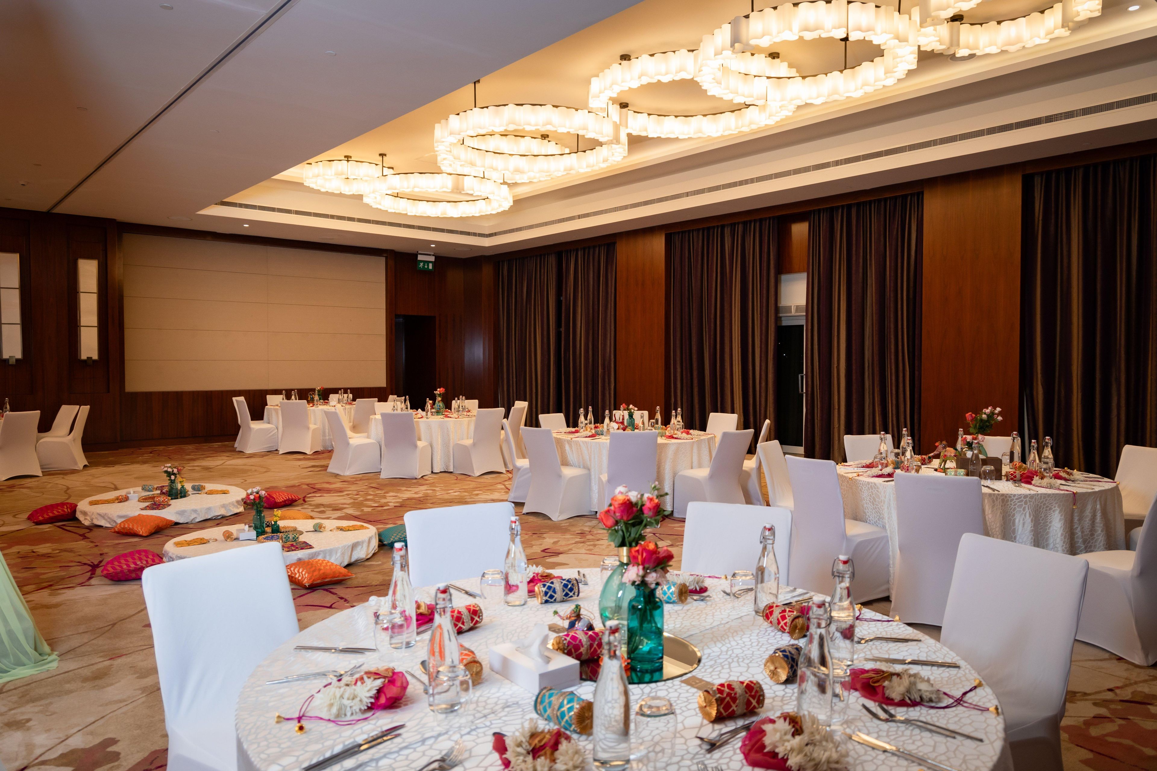 Un salón de banquetes con mesas redondas, sillas blancas y candelabros.