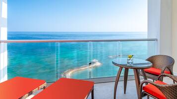 A balcony with a glass railing overlooking a turquoise sea and a clear sky.