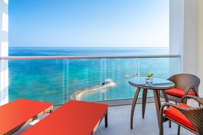 Varanda com guarda-corpo de vidro e vista para um mar azul-turquesa e céu claro.