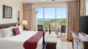 A hotel room with a bed, a TV, a balcony with a view of the ocean, and a ceiling fan.