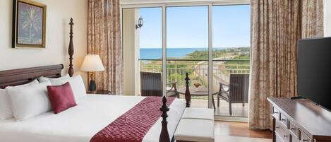 Habitación de hotel con cama, televisor, balcón y vista al océano, además de ventilador de techo.