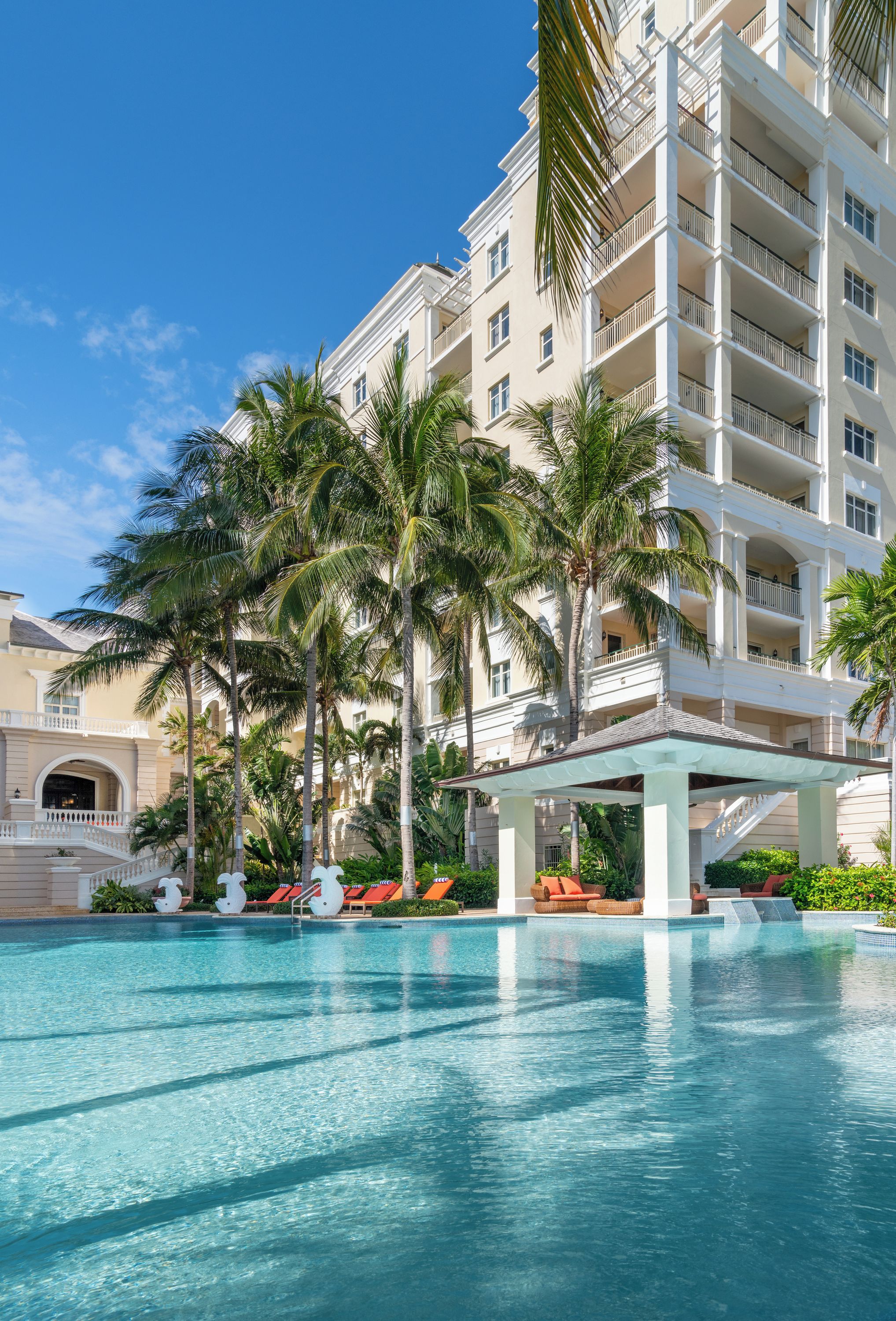 A hotel with a pool, palm trees, and a multi-story building.