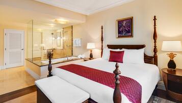 A hotel room with a large bed, a separate sitting area, a bathroom with a glass shower enclosure, and a large mirror.