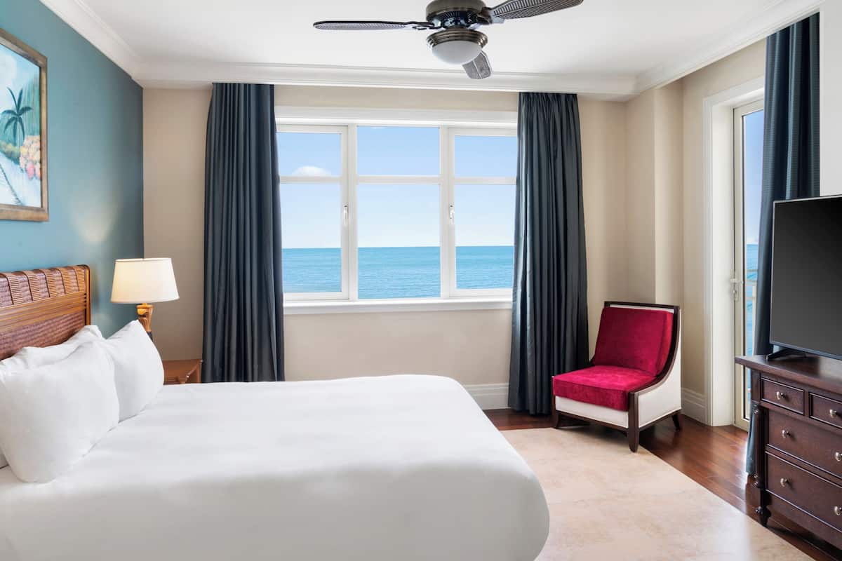 Habitación de hotel con una cama grande, televisión, una silla roja y vista al mar.