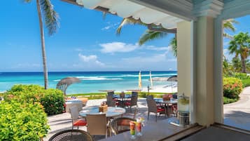 A beachside patio with outdoor seating, a view of the ocean, and a clear sky.