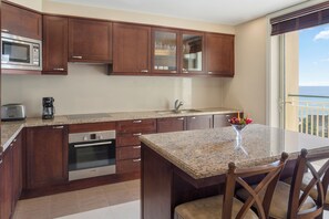 A modern kitchen with wooden cabinets, a granite countertop, a built-in oven, a coffee maker, and a view of the ocean through a balcony. - Jewel Grande Montego Bay Resort&spa (Montego Bay)